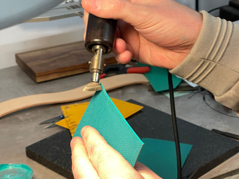 A close up of a person trimming aqua coloured leather at a leather work class